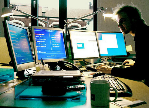 Άνδρας εργάζεται μπροστά σε τρεις οθόνες υπολογιστή