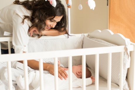 Γυναίκα πάνω από κούνια με μωρό- Μάθετε στο παιδί σας να κοιμάται όλη τη νύχτα.