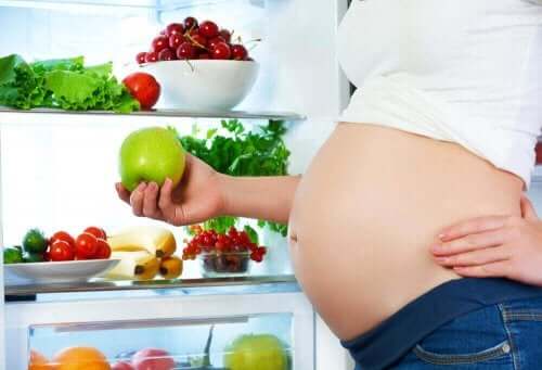 Έγκυος μπροστά σε ψυγείο κρατά μήλο