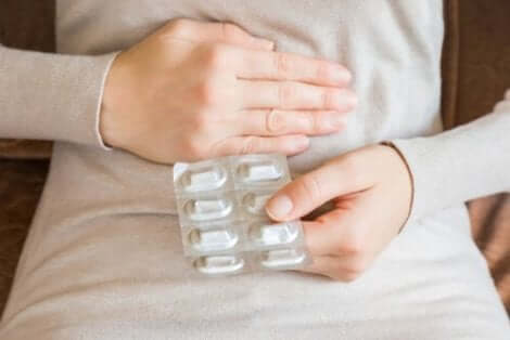 Γυναίκα πιάνει το στομάχι της και κρατά φάρμακα