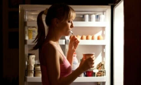 Γυναίκα τρώει μπροστά σε ανοιχτό ψυγείο